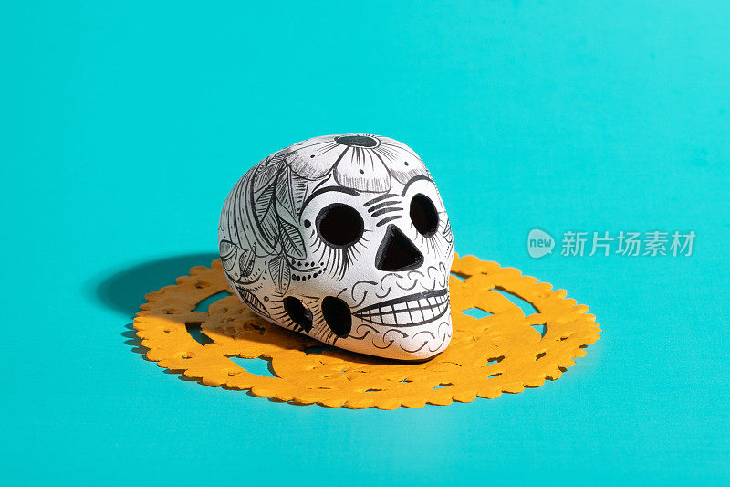 死亡的一天的陶器头骨(calavera)在黄色papel picado在蓝绿色的背景，Dia de Muertos的背景